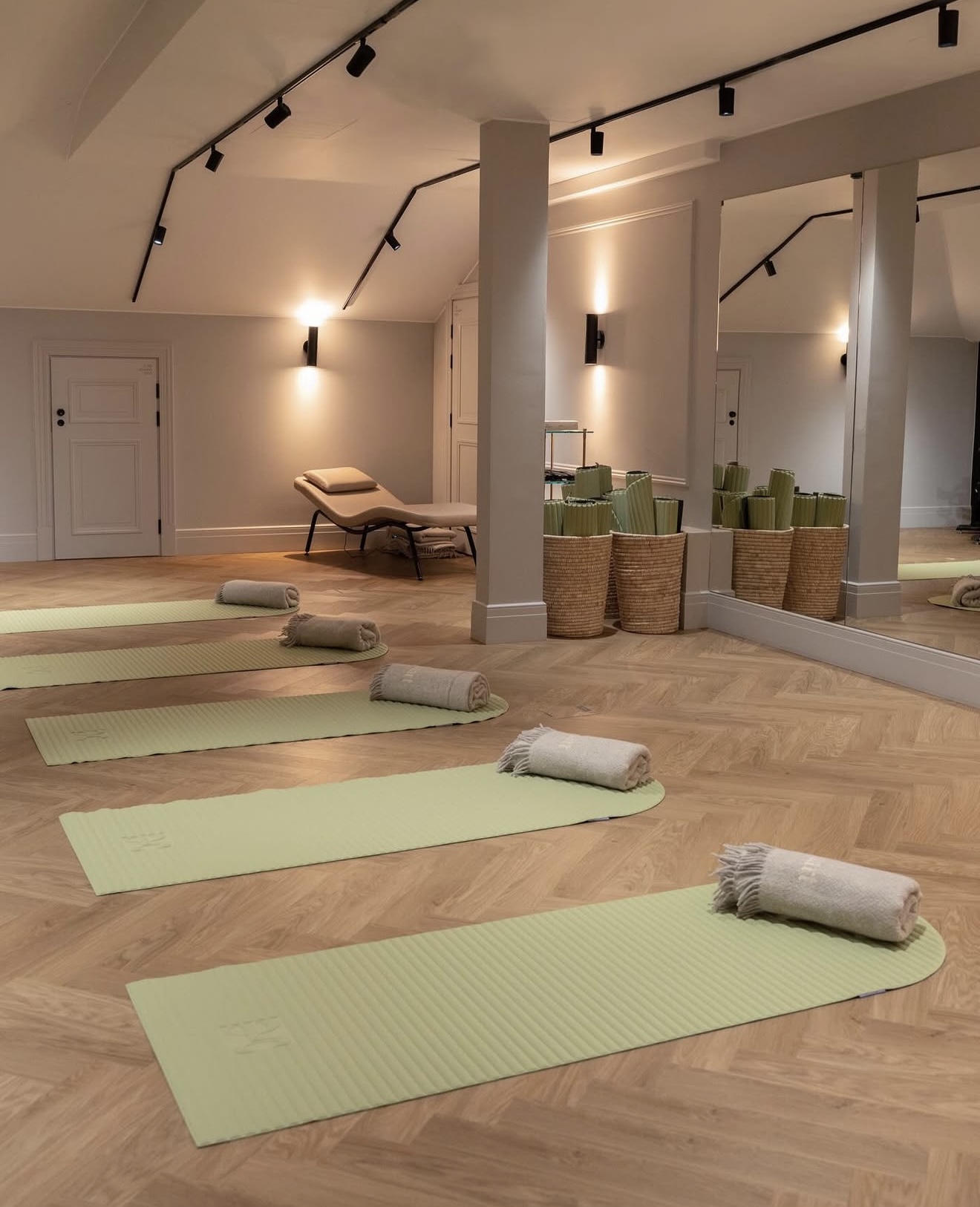 A studio floor at The Hotel Maria: pale green mats on herringbone parquet, a rolled towel on each.