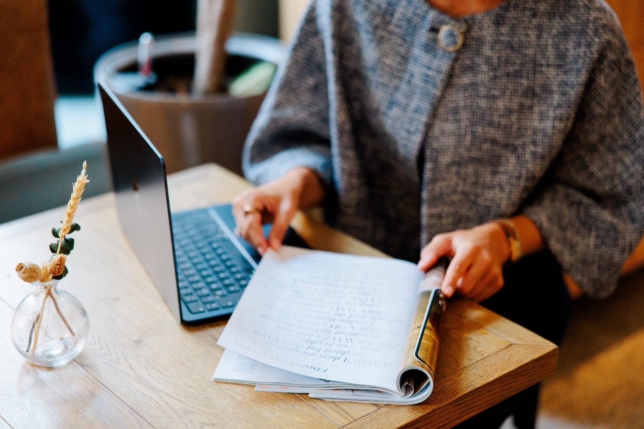 Hands turning the page of a notebook beside a laptop on a wooden table.