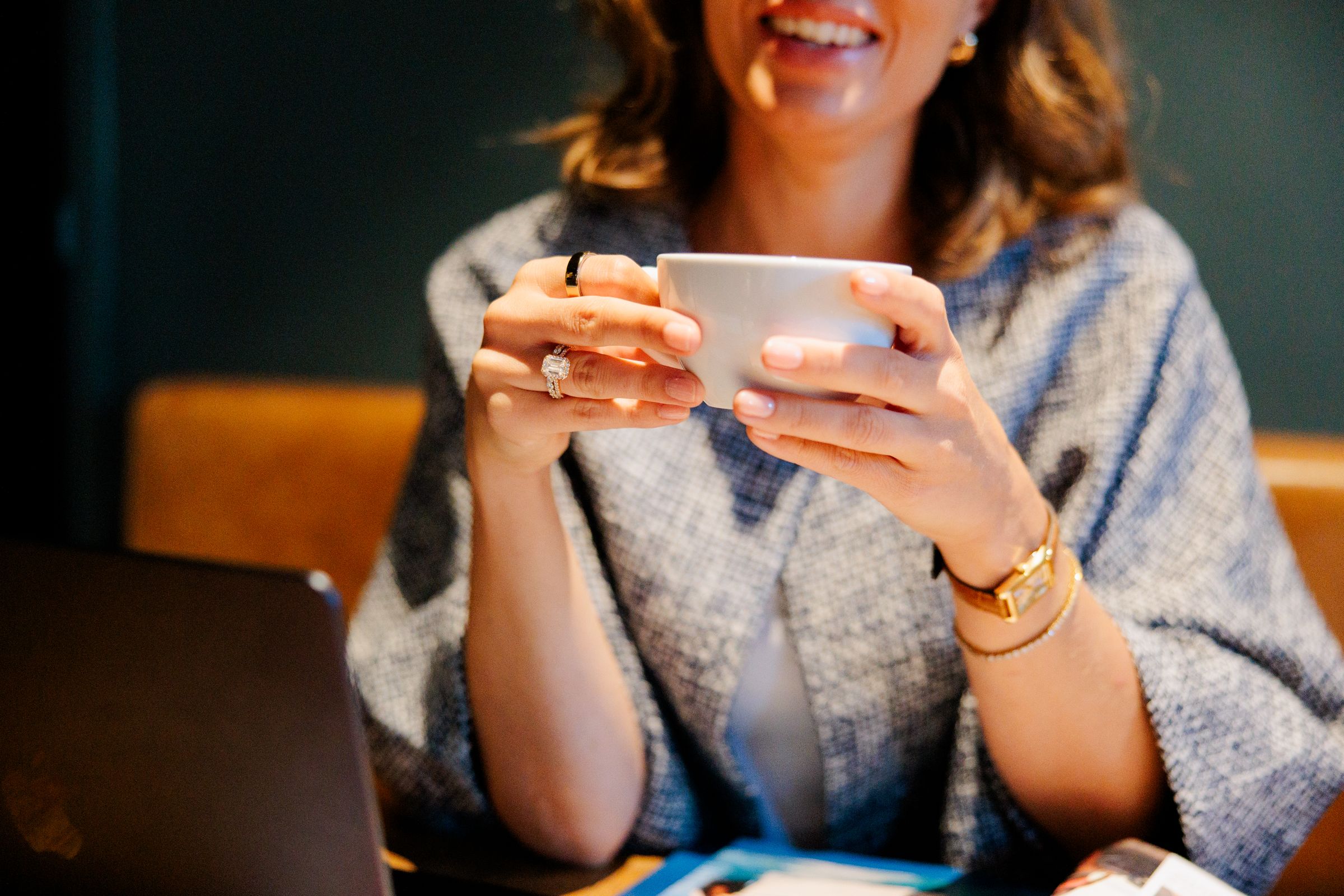 A coffee cup held in both hands, rings and gold bracelets, in warm light.